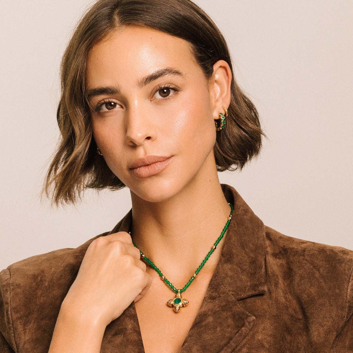 A woman with short brown hair models a green beaded necklace with a gold-toned floral pendant and matching green earrings against a plain light beige background.