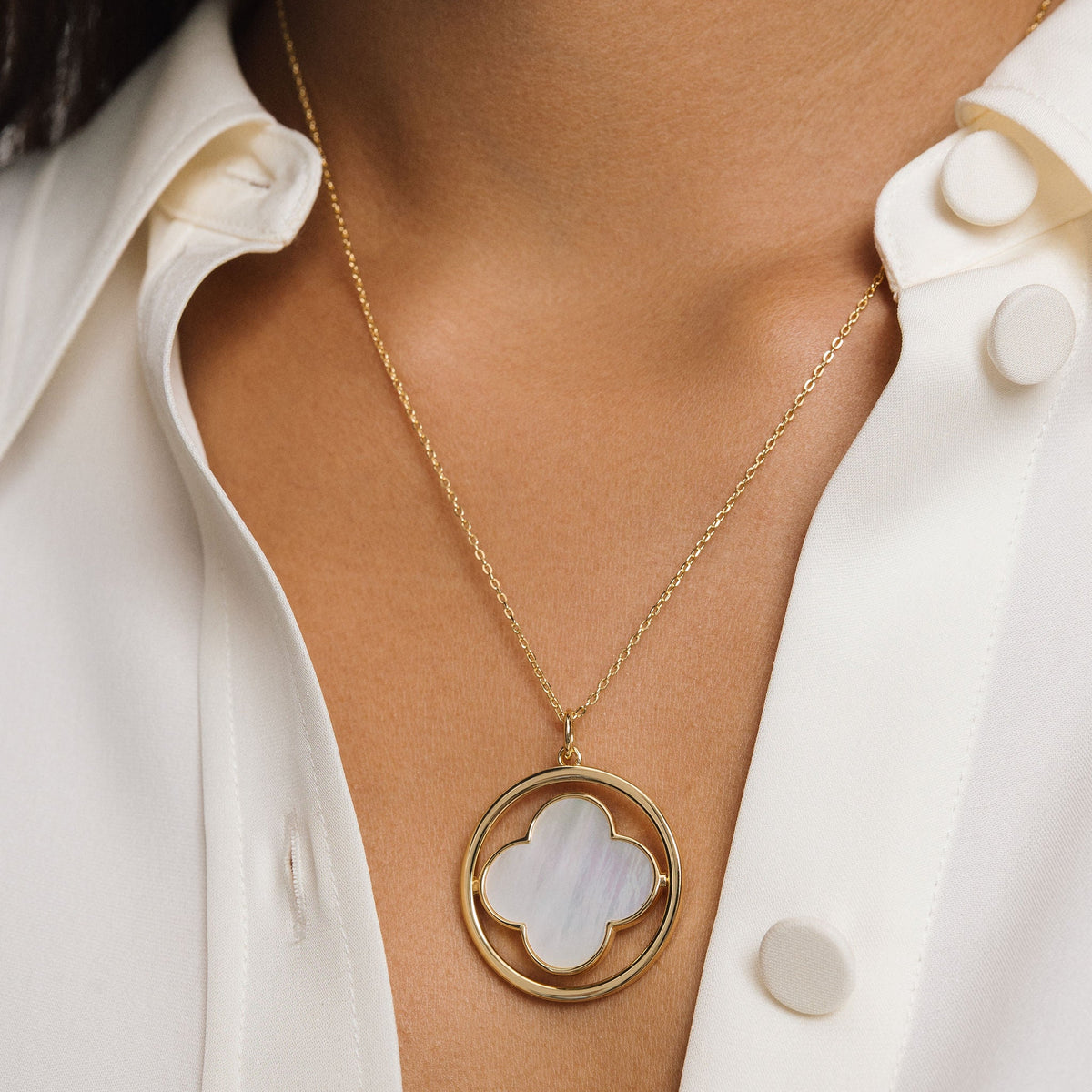Gold necklace with a clover pendant worn by a person in a white shirt.
